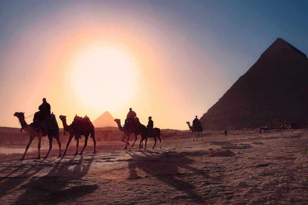 pessoas em camelos no entardecer, próximos às Pirâmides de Gizé